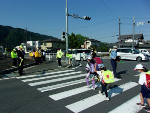 恵那市長、恵那警察署長、交通安全協会員らが横断歩行中の児童らを見守っている