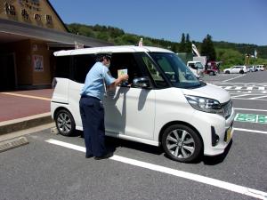 警察官が車に乗った道の駅利用者に対しチラシ等を渡している。
